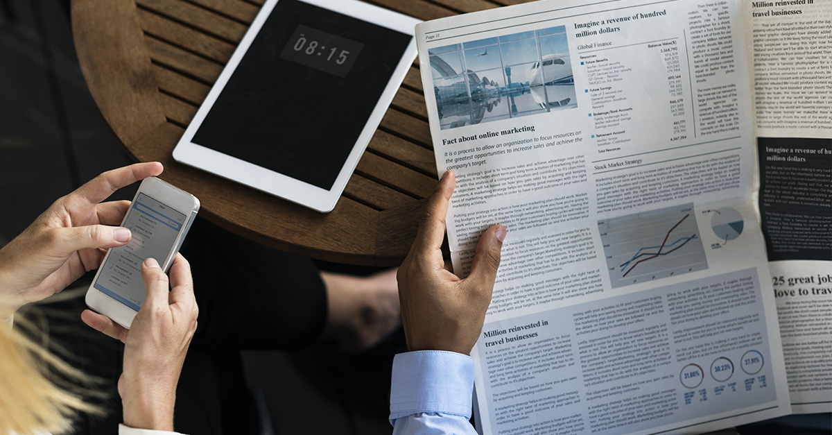 person holding newspaper and tablet on table