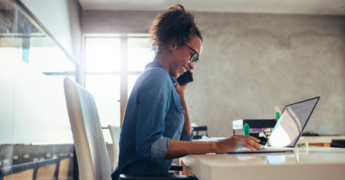 woman at desk on laptop using phone