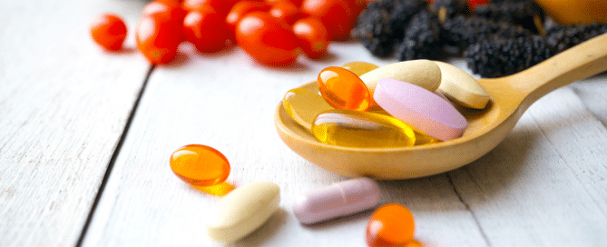 pills on a wooden spoon with produce in the background