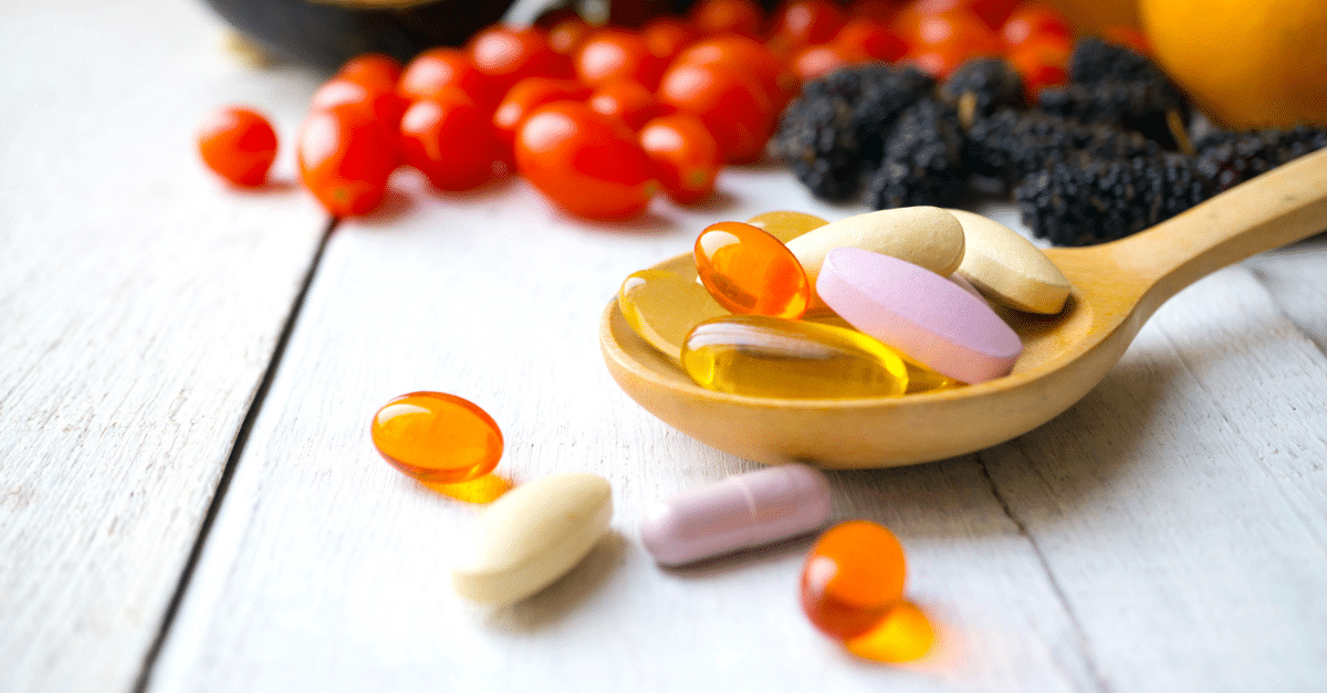 pills on a wooden spoon with produce in the background