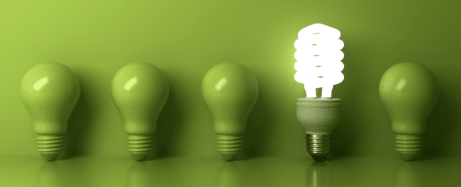 single lit lightbulb surrounded by green lightbulbs