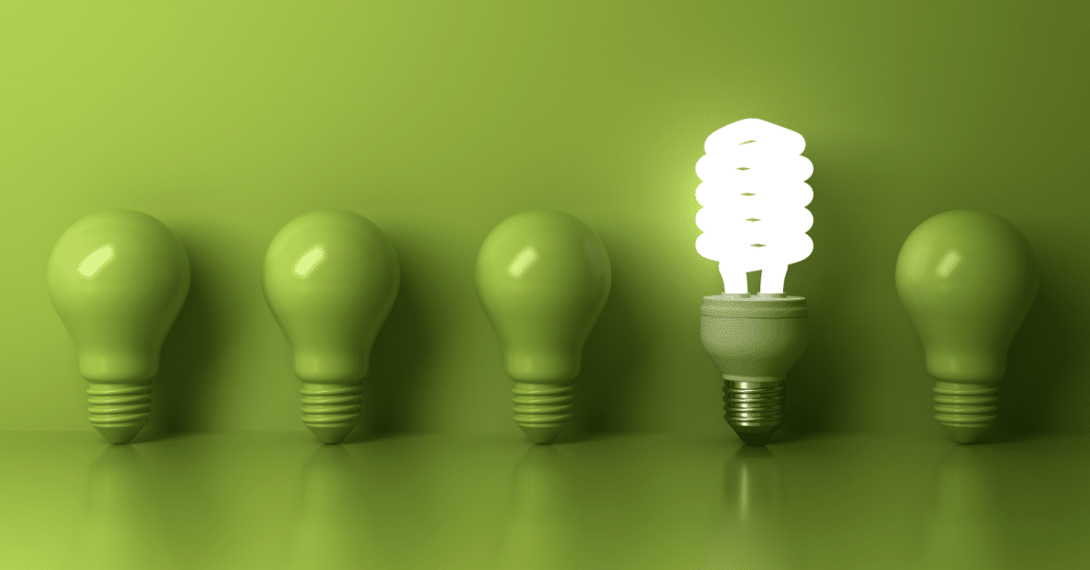 single lit lightbulb surrounded by green lightbulbs