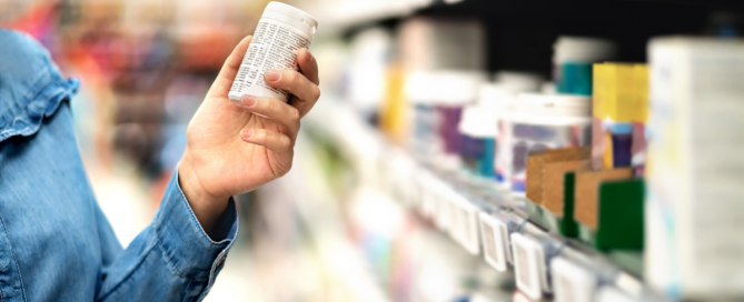 person holding pill bottle in store isle